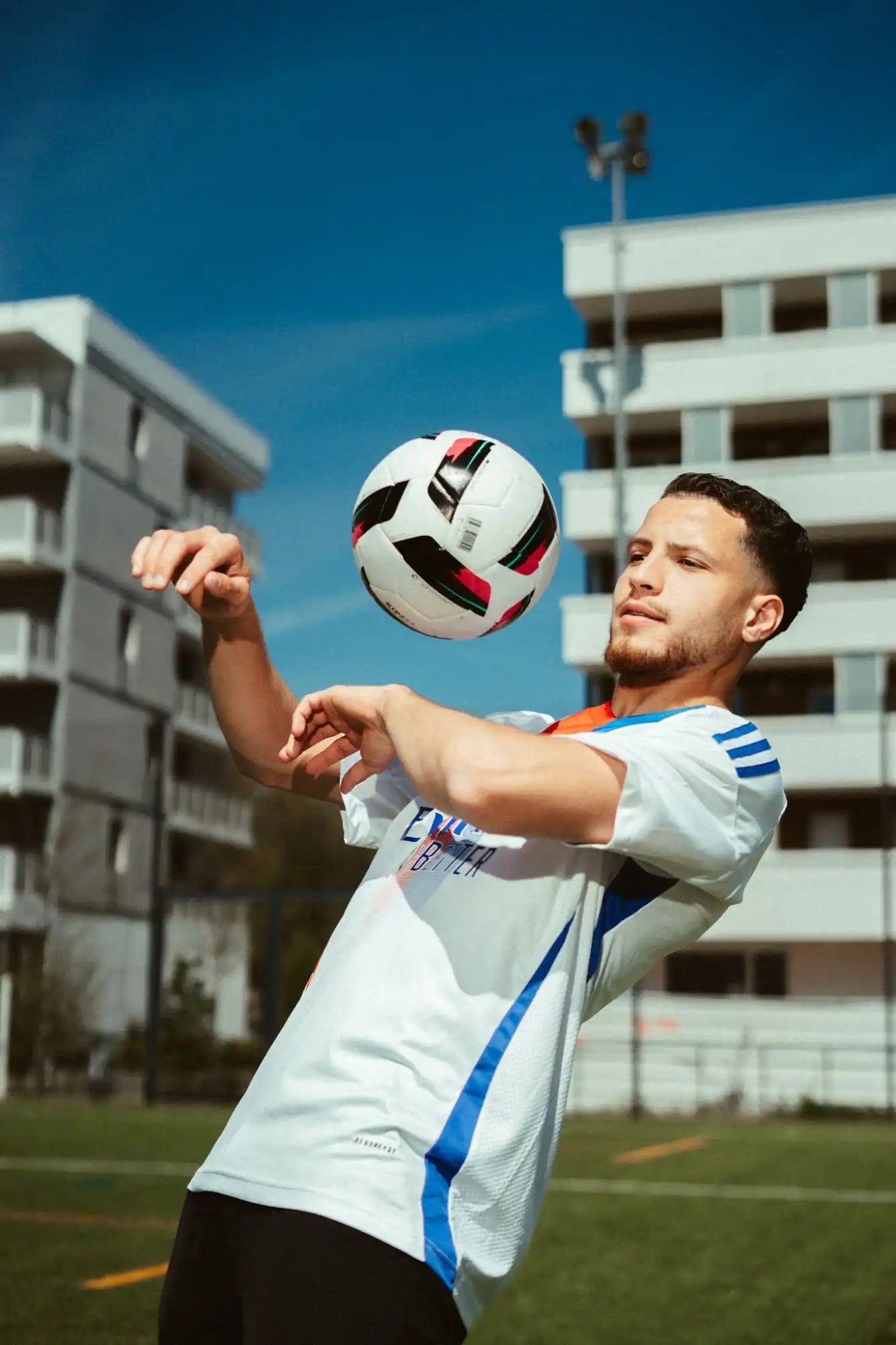 Un joueur de football en maillot blanc et bleu, réalisant un coup avec un ballon de football noir, blanc et rouge.